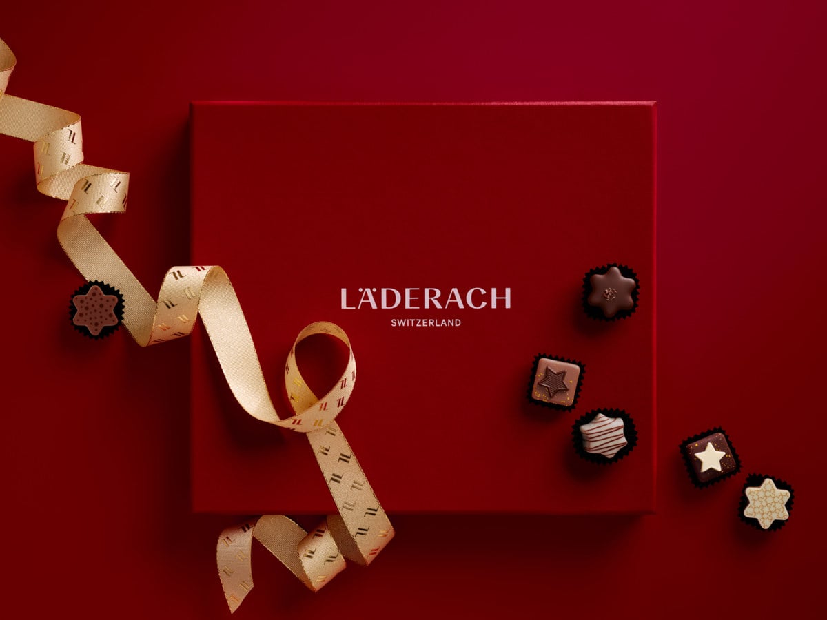 Red Läderach Christmas gift box tied with a gold ribbon, surrounded by star-shaped pralines